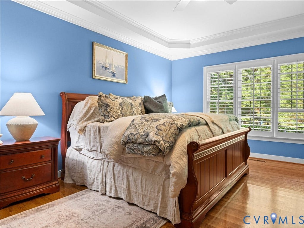 15706 Fox Marsh Drive, Moseley, VA 23120 Serene primary bedroom showcasing vibrant blue walls, hardwood flooring, and abundant natural light from triple-panel shuttered windows