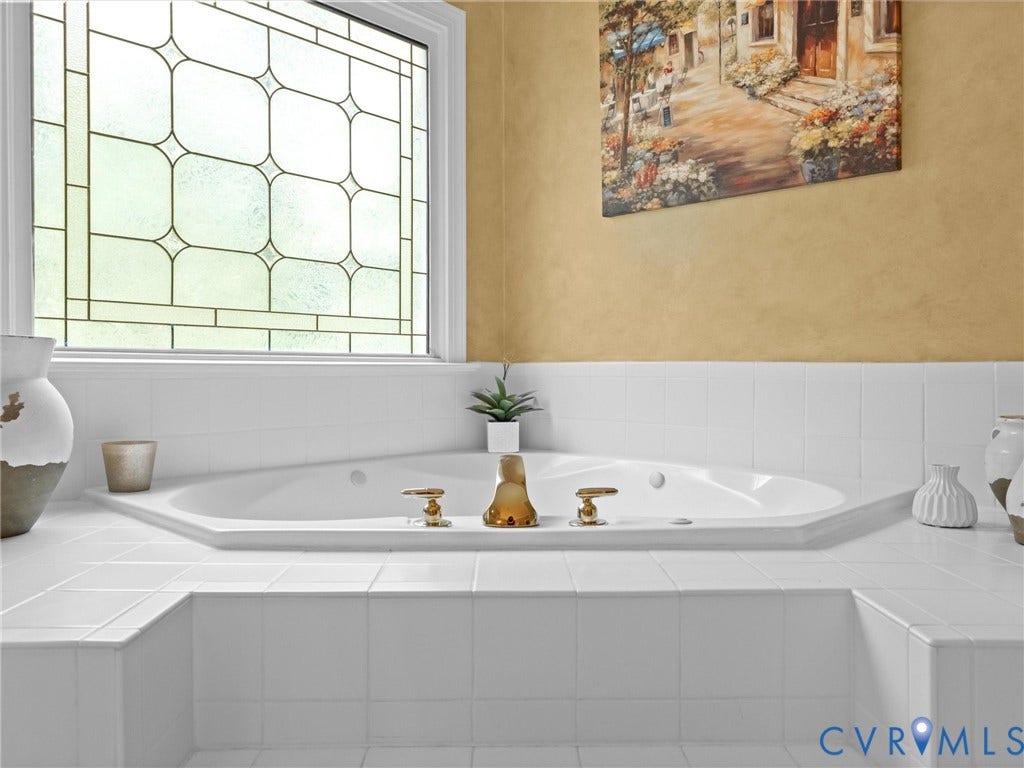15706 Fox Marsh Drive, Moseley, VA 23120 Built-in soaking tub with brass fixtures, surrounded by white tile, featuring a leaded glass window above