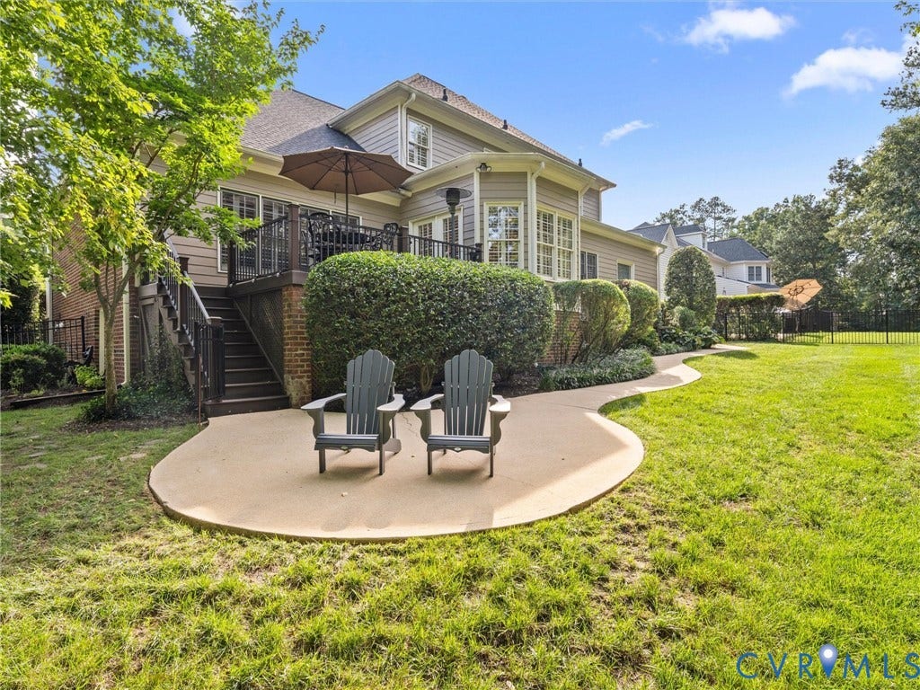 15706 Fox Marsh Drive, Moseley, VA 23120 Expansive lawn with a curved concrete patio, elevated deck with dark railings, and mature landscaping