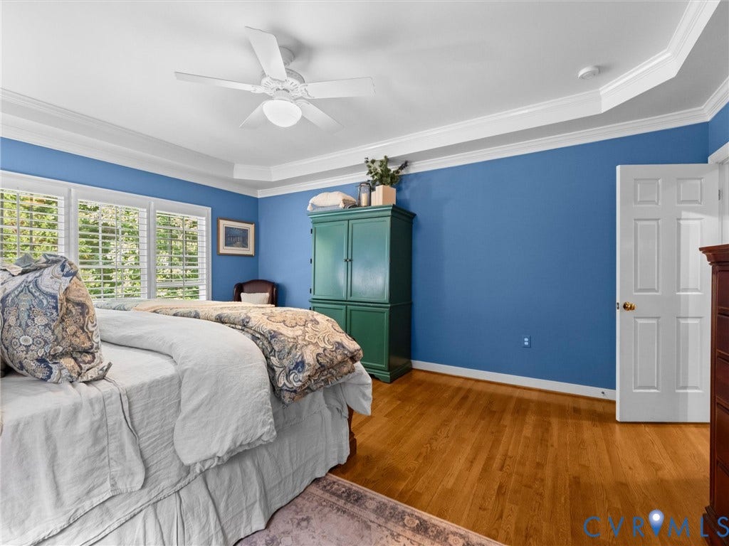 15706 Fox Marsh Drive, Moseley, VA 23120 Bright primary bedroom showcasing vibrant blue walls, wood-finish flooring, and abundant natural light from multi-pane shuttered windows