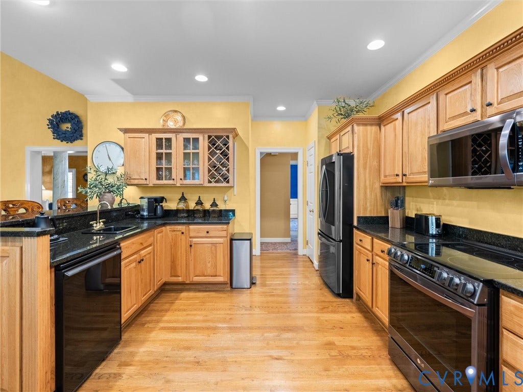 15706 Fox Marsh Drive, Moseley, VA 23120 Galley-style kitchen featuring warm wood cabinetry with glass-front upper cabinets, black stainless steel appliances, black granite countertops, recessed lighting, and hardwood flooring throughout the open layout
