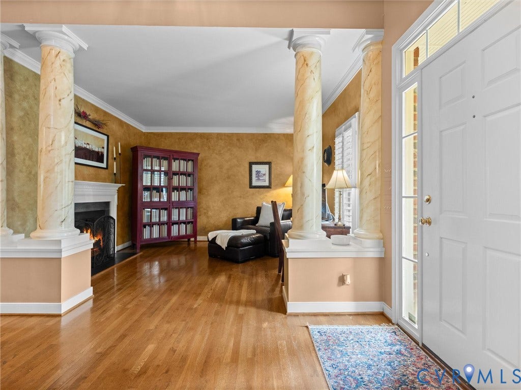 15706 Fox Marsh Drive, Moseley, VA 23120 Hardwood flooring, decorative columns, white paneled entry door, transom window, and a fireplace with a mantel