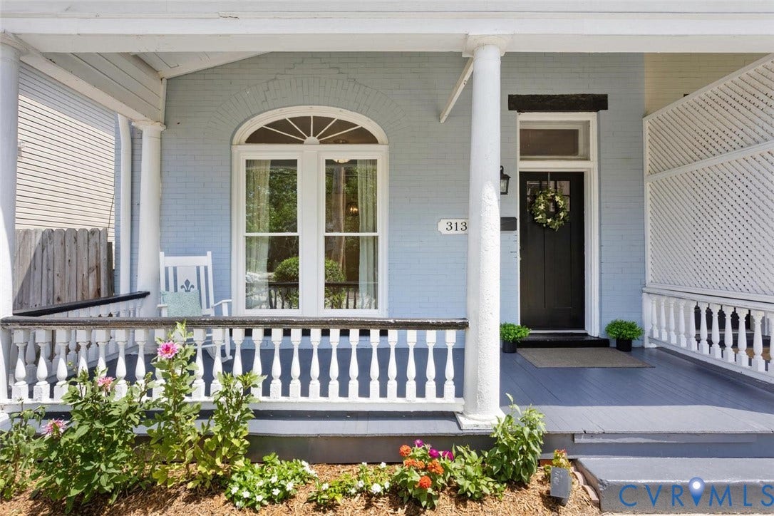 313 W 27th Street, Richmond, VA 23225 Covered front porch with white baluster railing, light blue painted brick exterior, arched transom window, and dark paneled entry door
