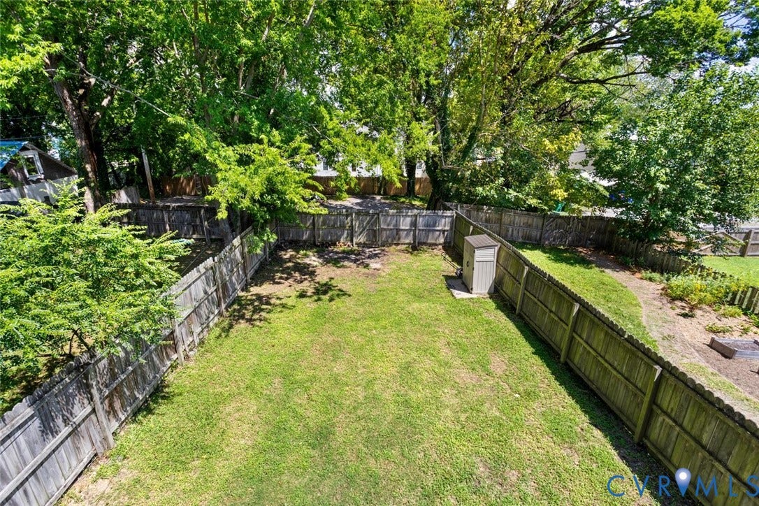 313 W 27th Street, Richmond, VA 23225 Expansive yard featuring a wooden privacy fence, mature trees, manicured lawn, and a storage shed
