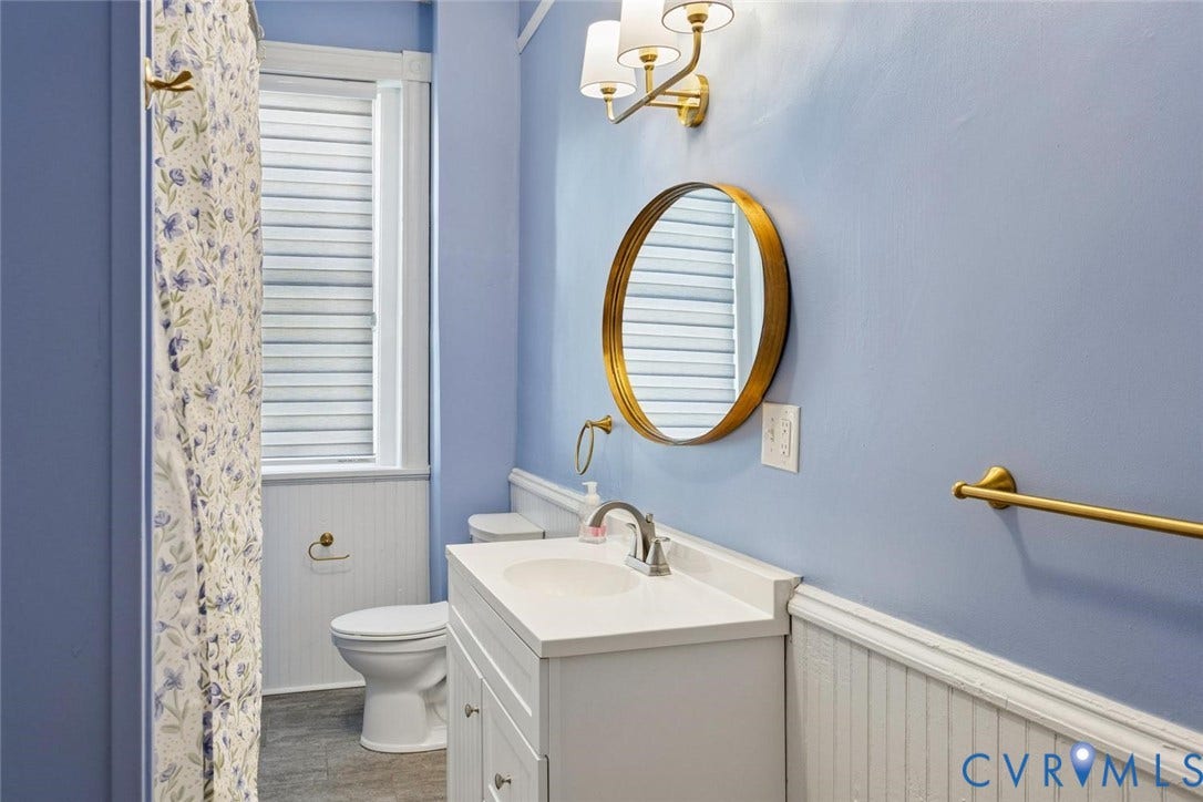 313 W 27th Street, Richmond, VA 23225 White vanity with a single basin sink, gold-toned wall sconce, and round gold-framed mirror