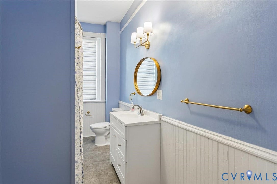 313 W 27th Street, Richmond, VA 23225 White vanity with an integrated sink, gold-finish hardware, a circular mirror, and beadboard wainscoting
