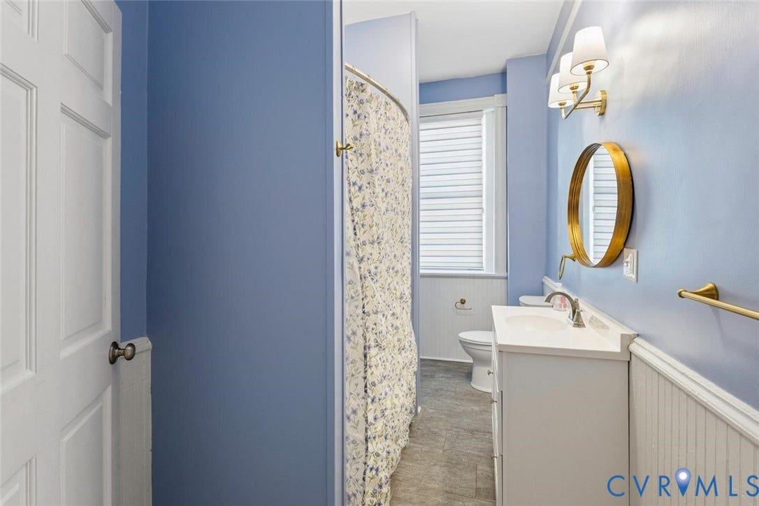 313 W 27th Street, Richmond, VA 23225 Vanity with integrated sink, gold-tone mirror, three-light sconce, beadboard wainscoting, and tile flooring