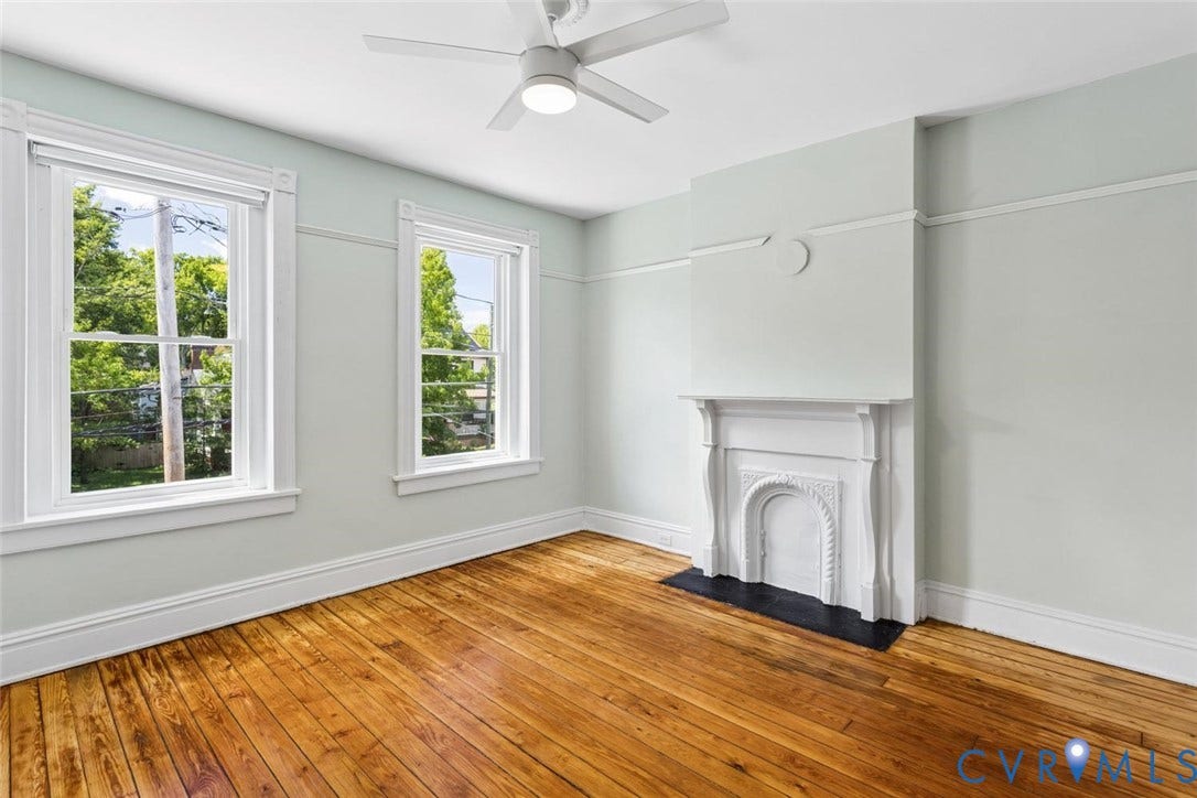 313 W 27th Street, Richmond, VA 23225 Wood-finish flooring, white ceiling fan with integrated lighting, two double-hung windows, and a decorative fireplace with a black hearth