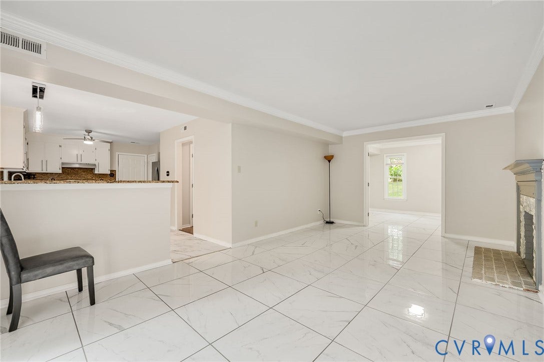 4820 Cedar Cliff Road, Chester, VA 23831 Spacious living area featuring large format tile flooring, crown molding, a fireplace, and a partial wall separating a kitchen with white cabinetry