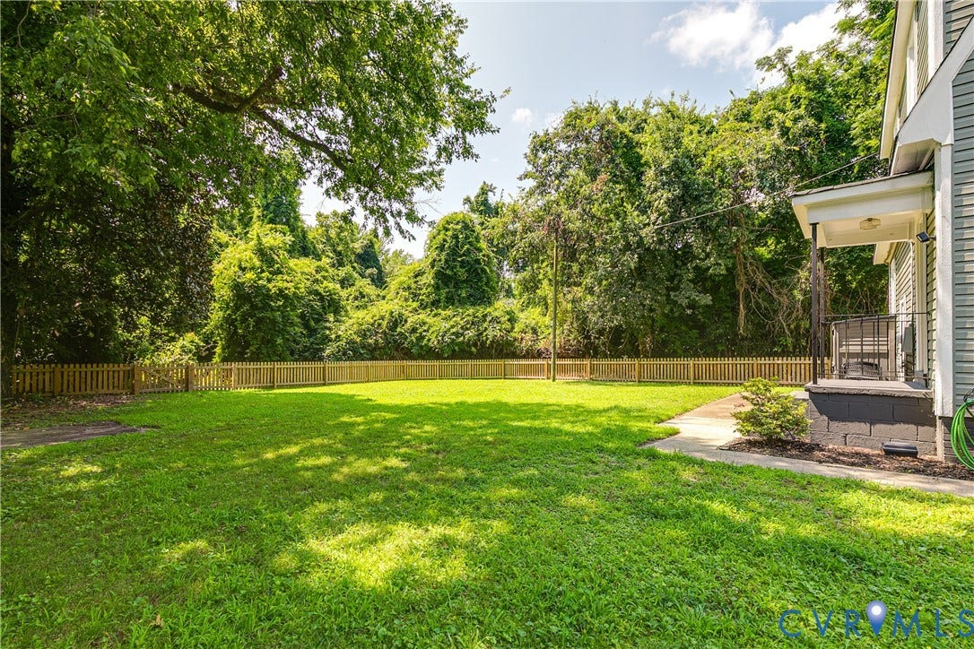 3215 Detroit Avenue, Richmond, VA 23222 Expansive lawn area with a wood picket fence, mature trees, and a concrete pathway leading to a covered porch with dark railing