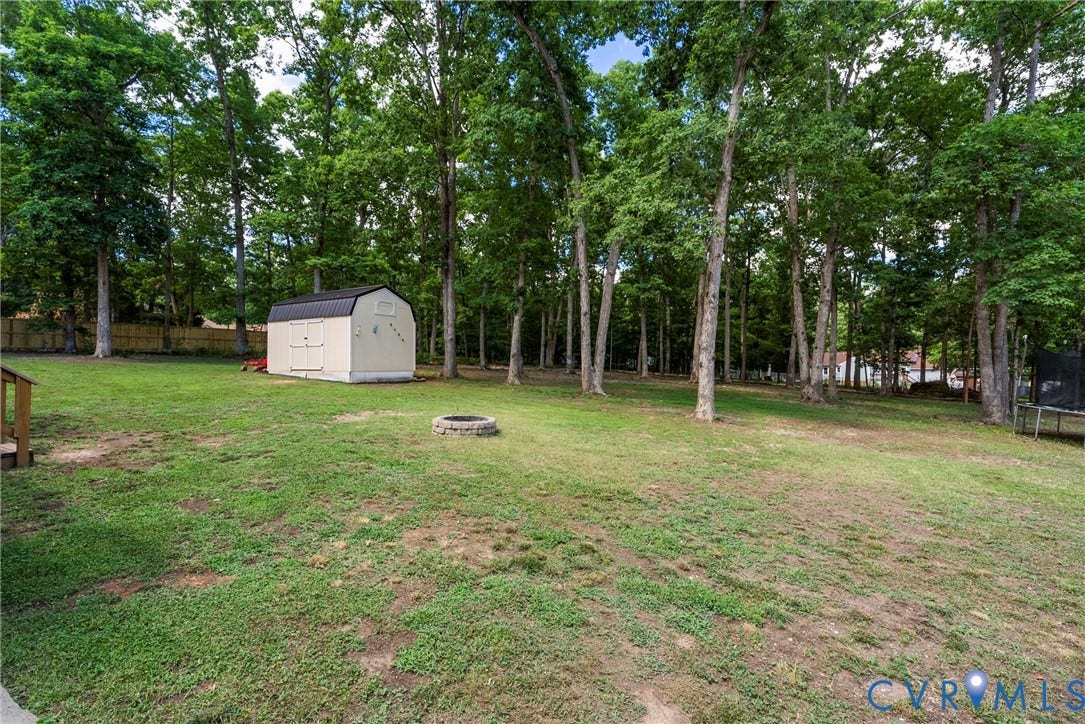 3242 Sherwood Ridge Drive, Powhatan, VA 23139 Expansive grassy yard featuring a detached storage shed with a gambrel roof, mature trees, and a stone-lined fire pit