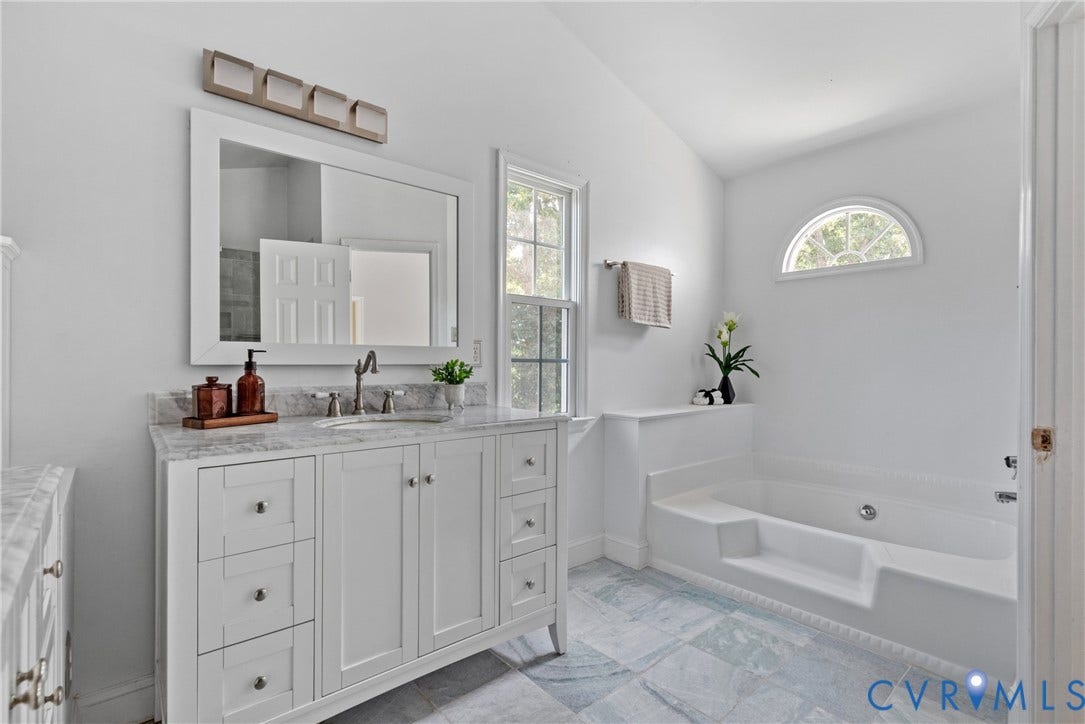 3242 Sherwood Ridge Drive, Powhatan, VA 23139 White vanity with a stone countertop and integrated sink, framed mirror, wall-mounted light fixture, white soaking tub, and arched transom window