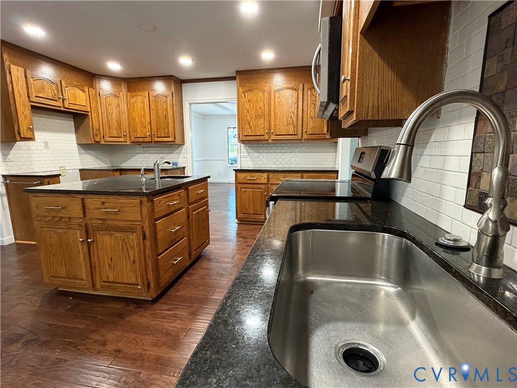 4603 Edenton Place, Greenbriar, Chester, VA 23831 Kitchen featuring wood-finish cabinetry, dark countertops, a center island with sink, a stainless steel sink, and white subway tile backsplash
