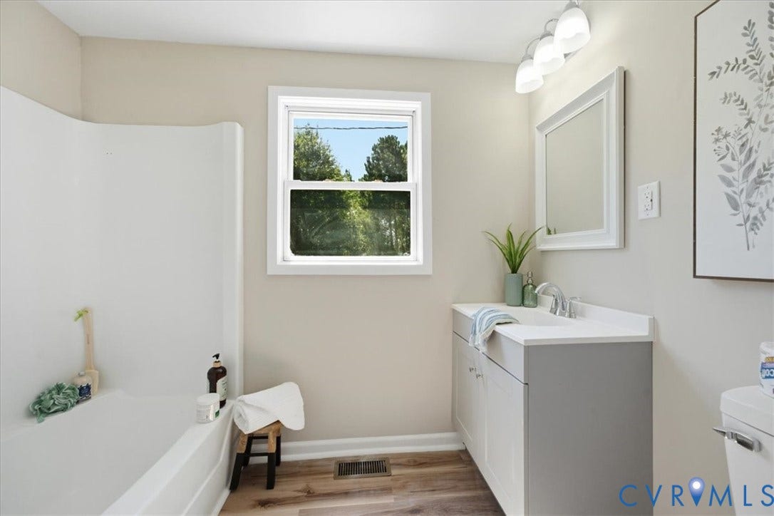 16111 Walkers Mill Road, Stony Creek, VA 23832 Integrated bathtub with shower, single window, wood-finish flooring, vanity with white countertop, and wall-mounted light fixture