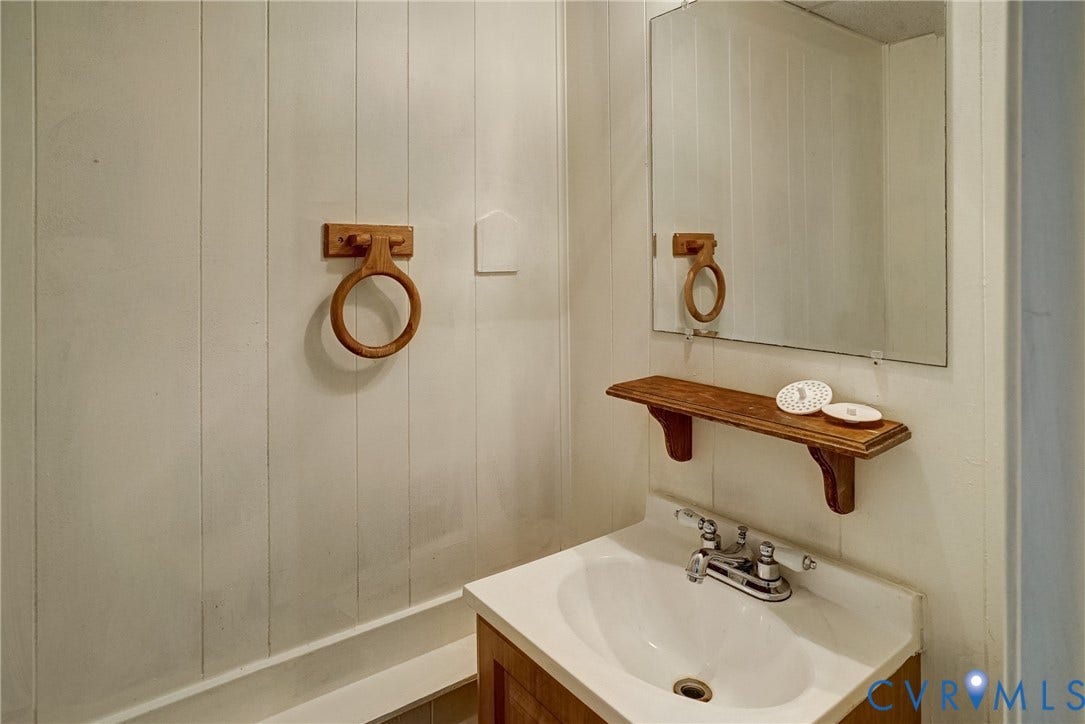 10104 Terry Court, Henrico, VA 23228 White paneled walls, a wall-mounted mirror, a wood-finish vanity with a white basin, and a wall-mounted wood-finish shelf