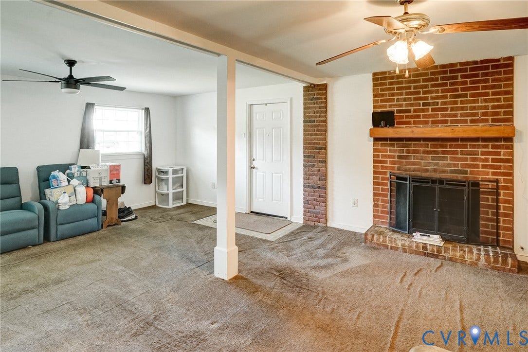 10104 Terry Court, Henrico, VA 23228 Spacious basement recreation area featuring exposed brick fireplace with dark metal doors, ceiling fans, neutral carpeting, and multiple support columns