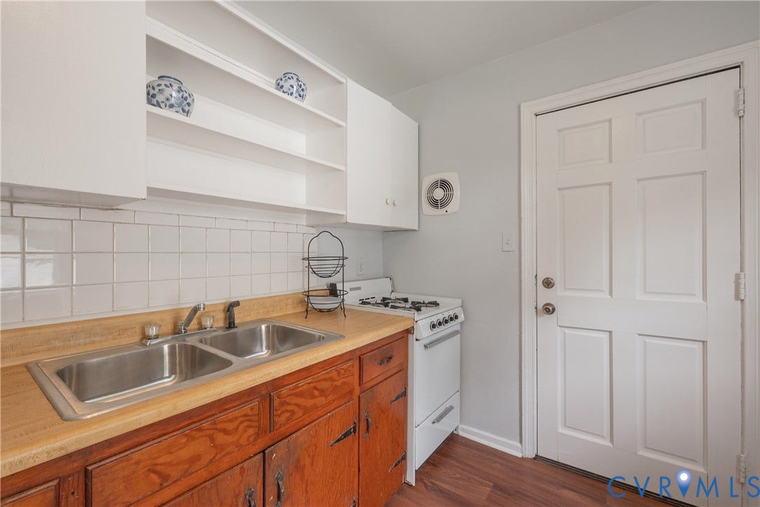 1704 Westhill Road, Richmond, VA 23226 Double basin stainless steel sink, wood-finish countertops, white tile backsplash, white upper cabinetry with open shelving, and rich wood-finish lower cabinetry and a gas range with yard access