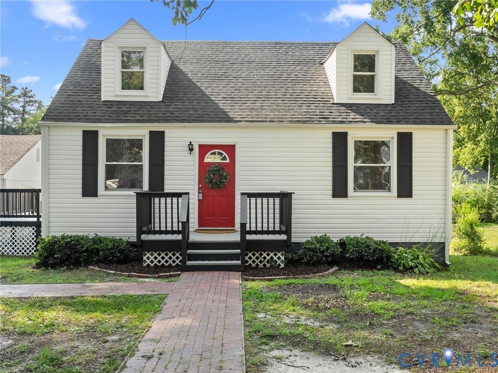 4818 Castlewood Road, Richmond, VA 23234 Classic Cape Cod-style home featuring white horizontal siding, a charming red entry door with wreath, and distinctive dormers with multi-pane windows