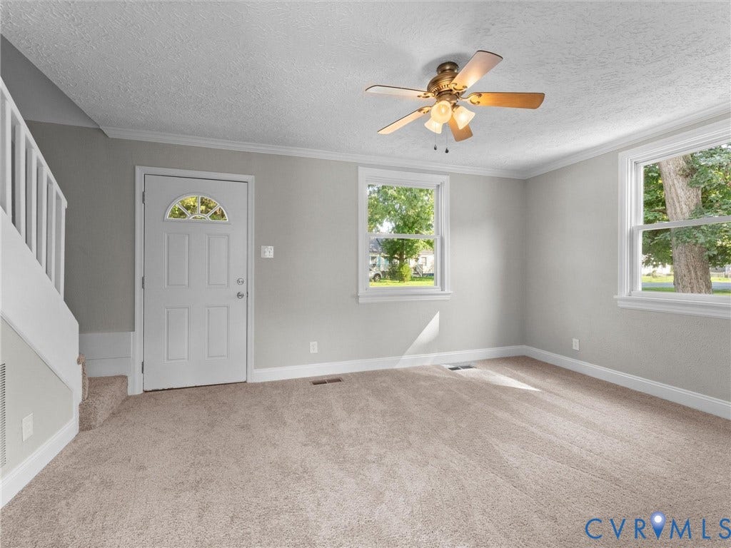 4818 Castlewood Road, Richmond, VA 23234 Bright, light-filled living space featuring neutral carpeting, multiple windows with natural light, ceiling fan with integrated lighting, and an open floor plan