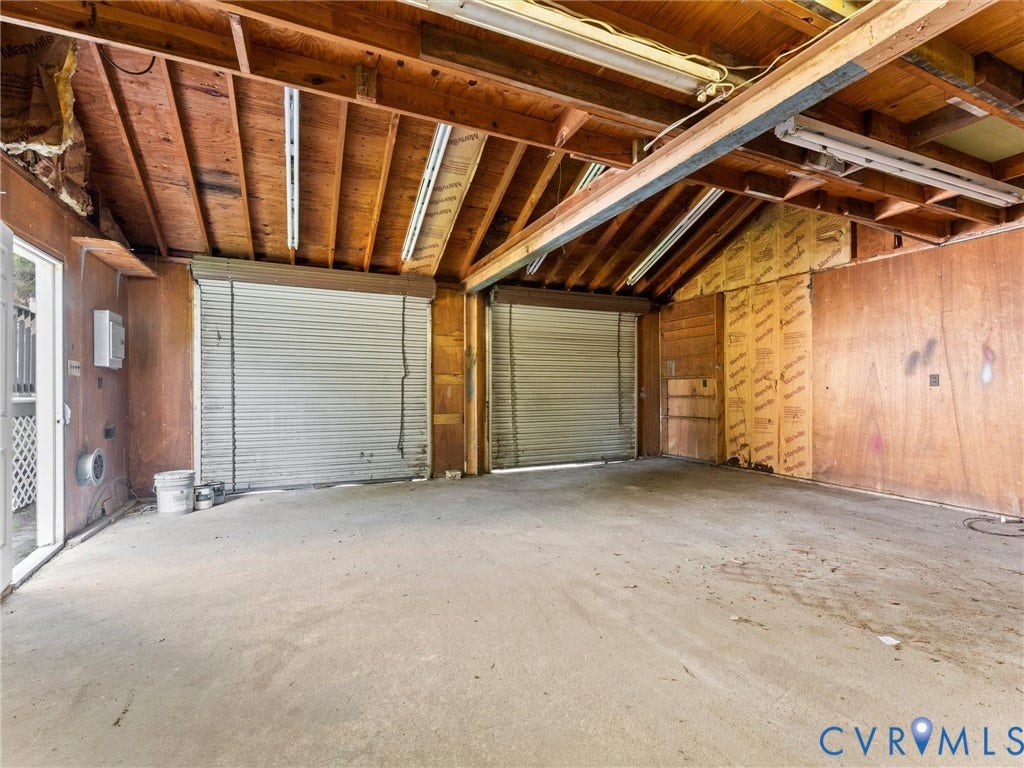4818 Castlewood Road, Richmond, VA 23234 Spacious garage featuring exposed wood beam ceiling, concrete flooring, and dual roll-up doors with metal security shutters