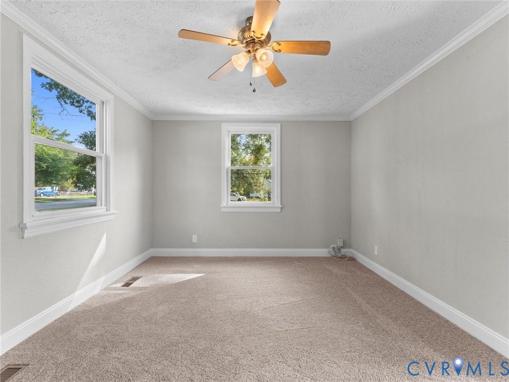 4818 Castlewood Road, Richmond, VA 23234 Bright and spacious bedroom showcasing dual windows with natural light, neutral wall finishes, neutral carpet flooring, and a ceiling fan with integrated lighting fixture