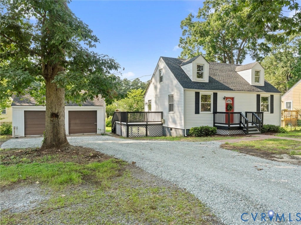 4818 Castlewood Road, Richmond, VA 23234 Charming farmhouse-style residence featuring a classic white exterior with dark roof accents, covered front porch with railings, and a two-car detached garage