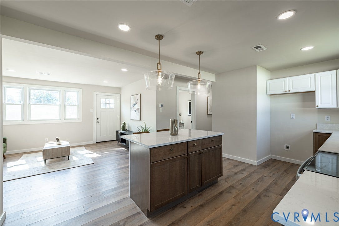 Open-concept living space with wood-finish flooring, recessed lighting, a kitchen island with a light-toned countertop, and white kitchen cabinetry