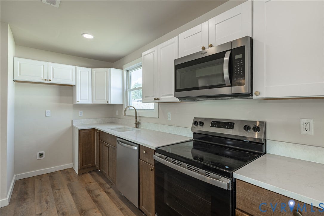 Kitchen featuring white upper cabinetry, wood-finish lower cabinetry, light-toned countertops, stainless steel appliances, and wood-finish flooring