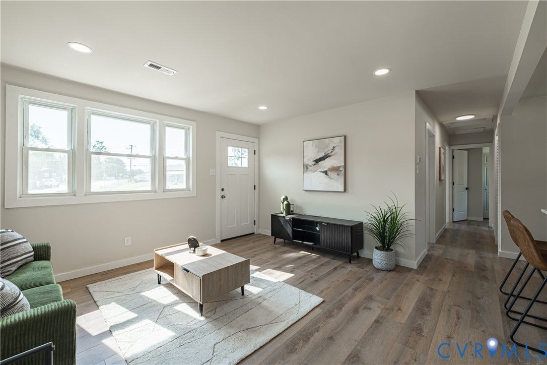 Wood-finish flooring, recessed lighting, multiple windows, a paneled entry door, and a hallway with a ceiling light