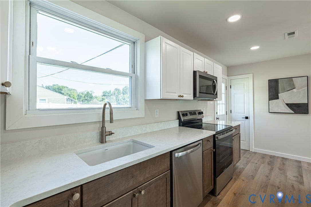 Contemporary kitchen featuring a white single-basin sink, stainless steel appliances, wood-finish flooring, white upper cabinetry, and dark wood-finish lower cabinetry