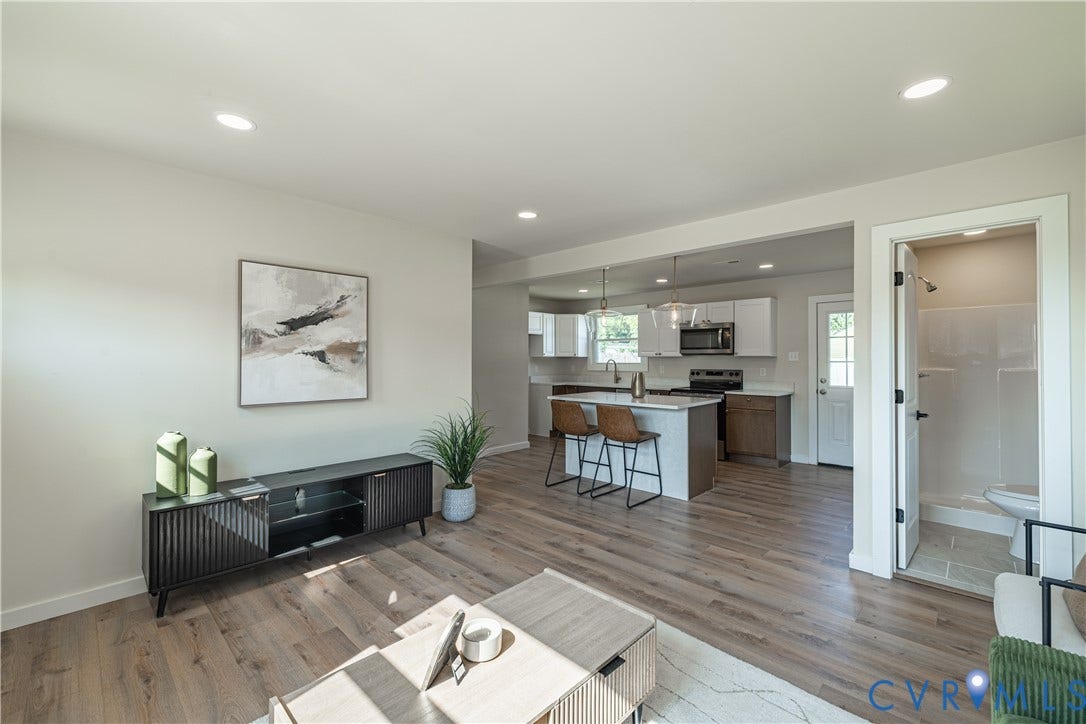 Open-concept living space featuring recessed lighting, wood-finish flooring, a kitchen island with seating, white shaker cabinetry, and a full bathroom with a shower