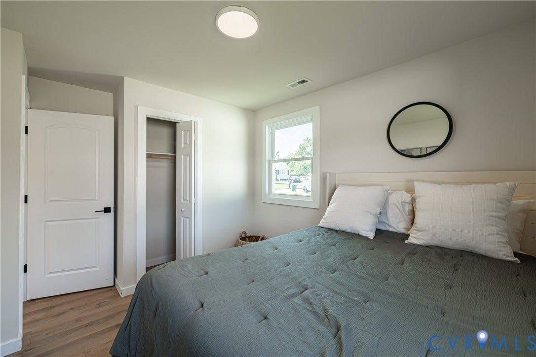 Wood-finish flooring, white paneled door with black hardware, bi-fold closet door, and a white framed window