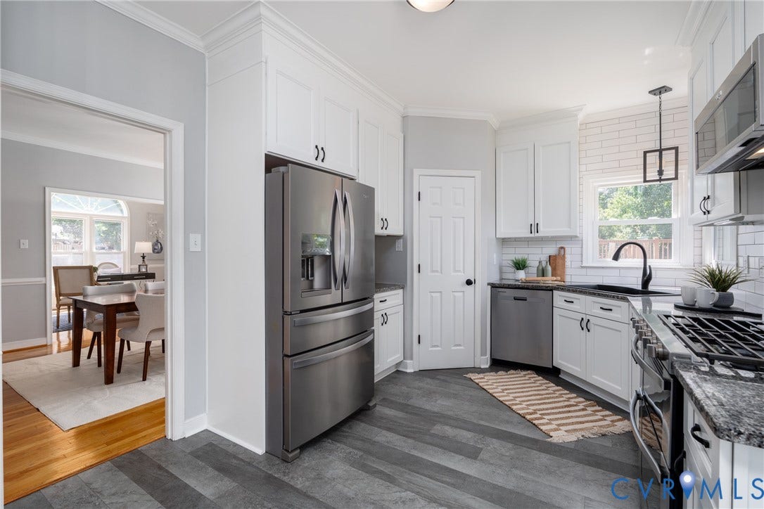 Kitchen featuring wood-finish flooring, white cabinetry, dark countertops, a white subway tile backsplash, and stainless steel appliances