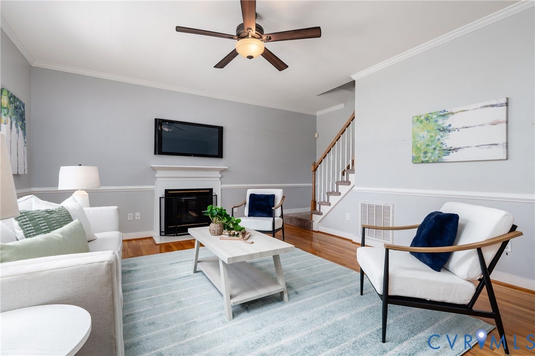 Hardwood-finish flooring, fireplace with white mantel, ceiling fan with integrated lighting, two-tone wall treatment, and white crown molding