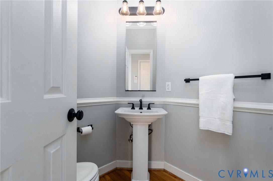 Pedestal sink with matte black faucet, wall-mounted mirror, and overhead lighting