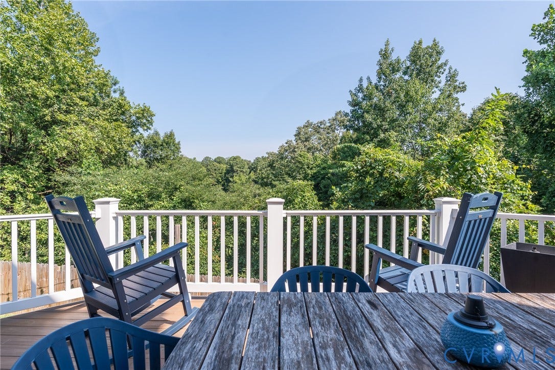 Expansive composite deck featuring multiple Adirondack-style seating areas, white vertical railings, and wood-finish decking that overlooks mature landscaping and wooded surroundings