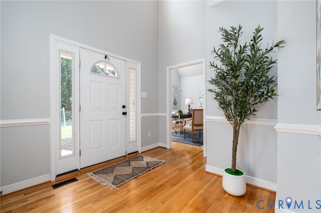 Double-height foyer with wood-finish flooring, white paneled entry door, and transom window