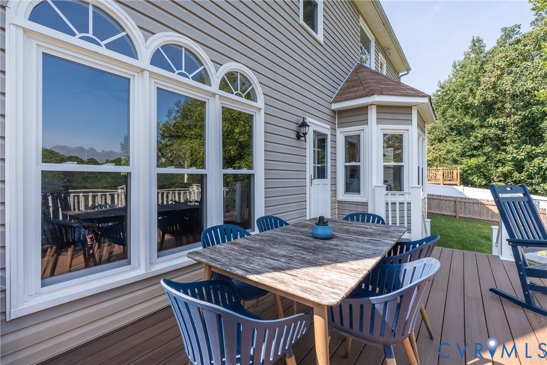 Expansive composite deck featuring a natural wood-finish dining table, blue Adirondack seating, and integrated lounge chairs overlooking manicured lawn and mature landscaping
