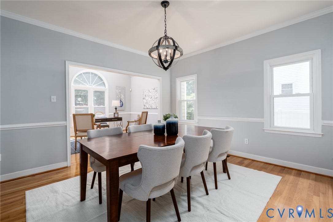 Hardwood flooring throughout, crown molding, chair rail detailing, recessed archway, and a modern chandelier
