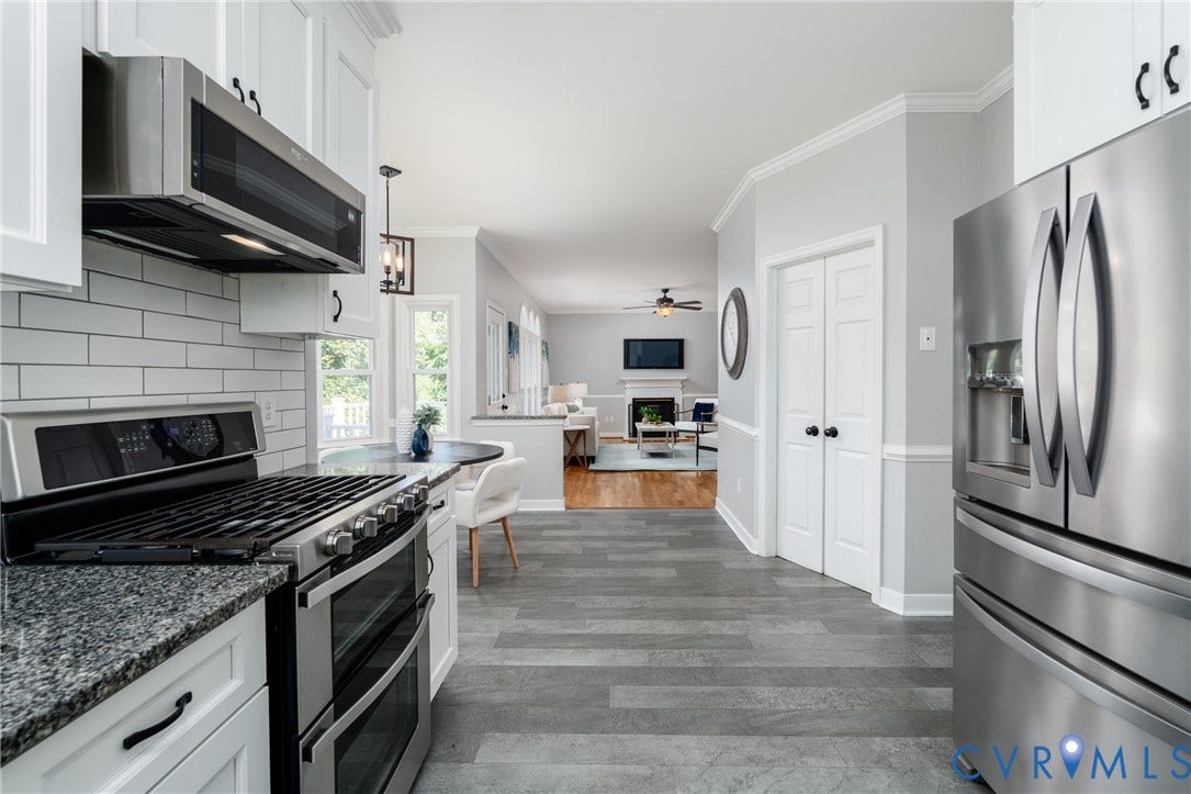 Stainless steel appliances, granite countertops, white cabinetry, subway tile backsplash, and wood-finish flooring