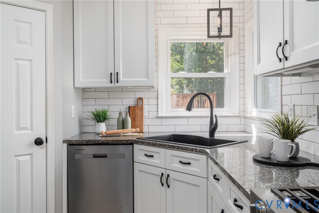 White shaker cabinetry, stainless steel dishwasher, black sink with gooseneck faucet, light granite countertops, and white subway tile backsplash