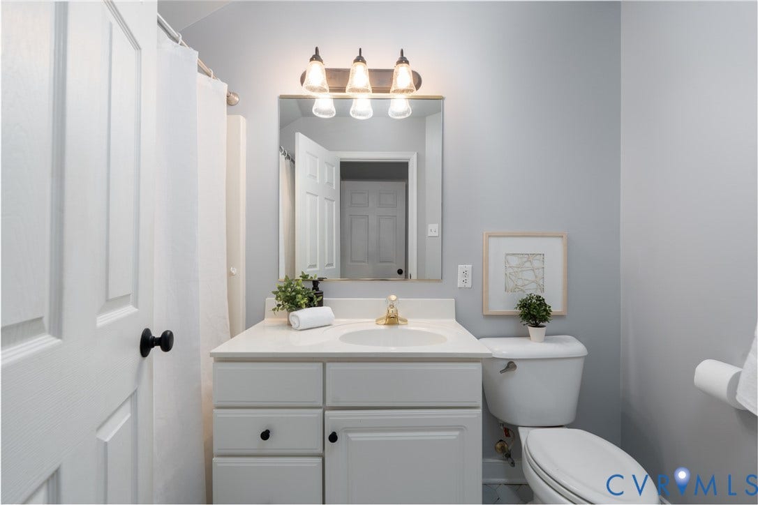 Bathroom with white vanity, integrated sink, brass fixtures, and framed mirror