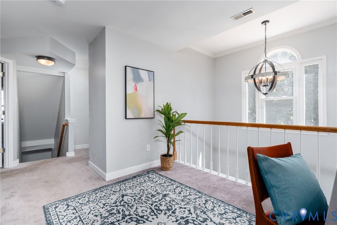 Bright upper-level landing featuring crisp white shiplap walling, wood-finish stair railing, and a patterned area rug