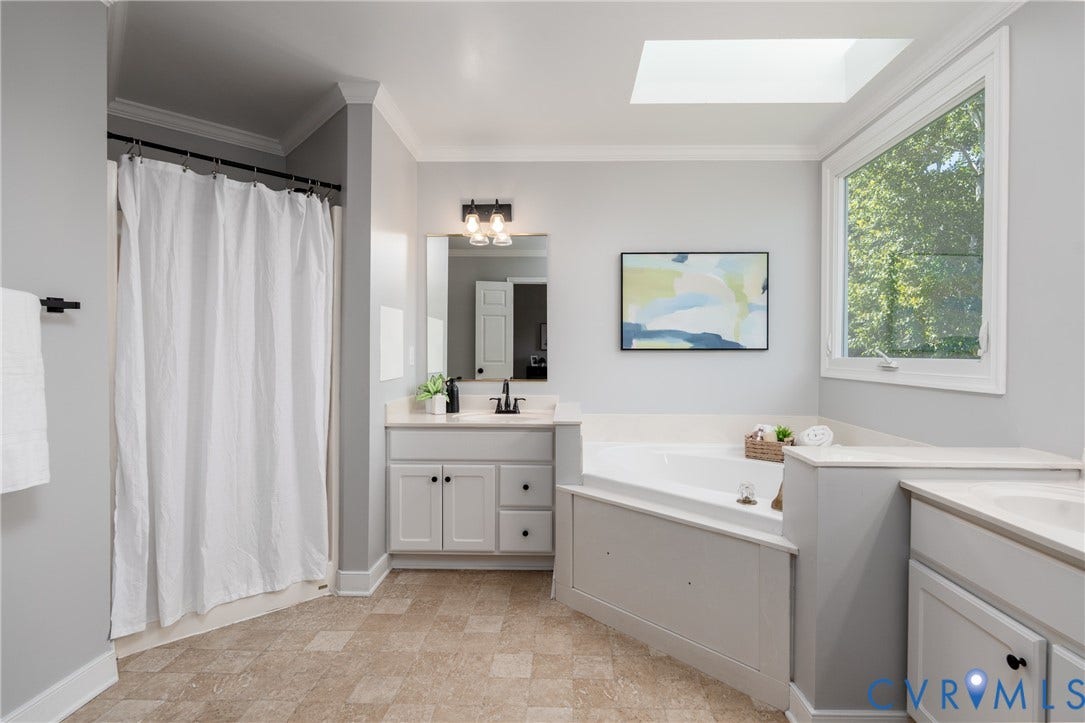 White built-in cabinetry, corner soaking tub, skylight, and large window
