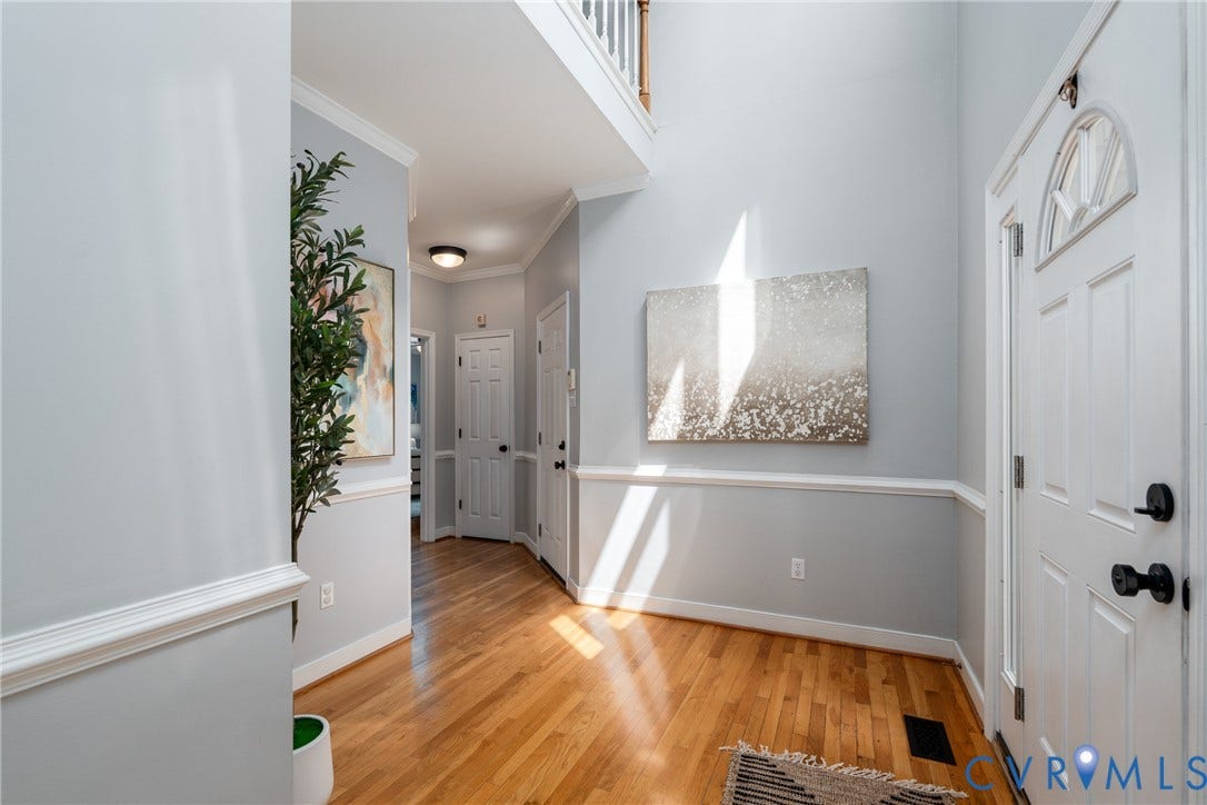 Two-story foyer with wood-finish flooring, white paneled entry door, and crown molding