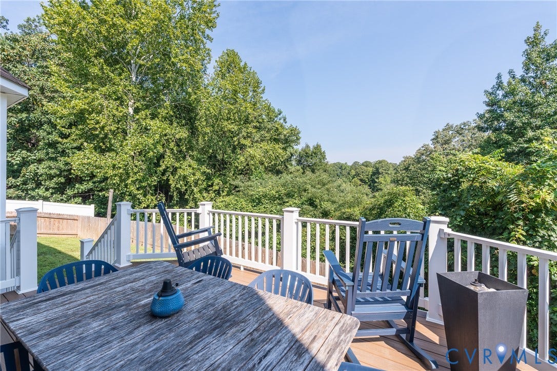 Expansive composite deck featuring composite wood-finish decking, white vinyl railings with decorative balusters, and integrated seating areas overlooking mature tree-lined landscaping