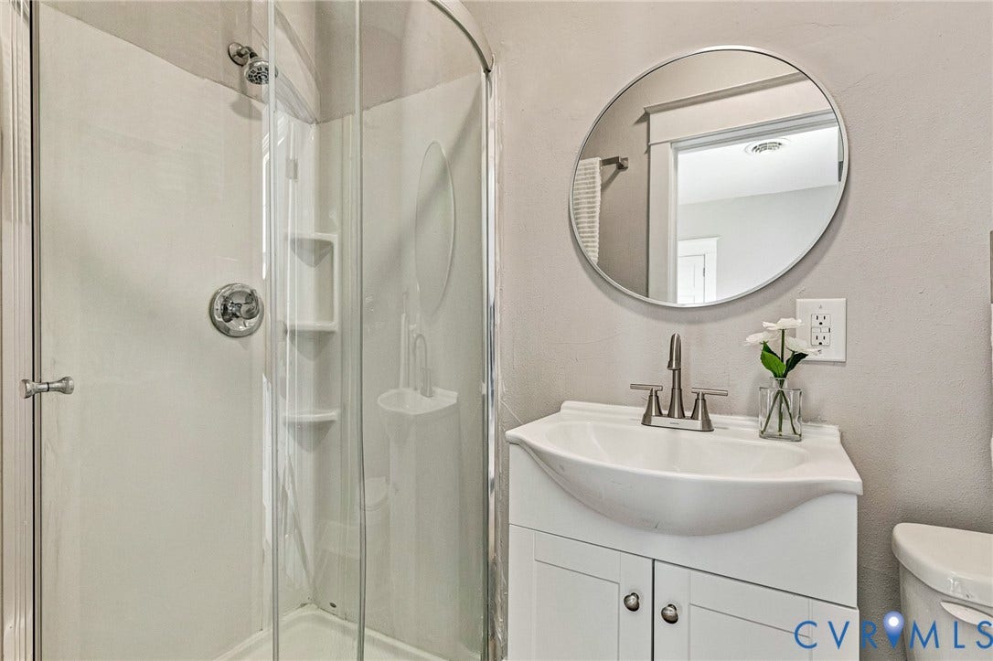 403 Masonic Lane, Masonic, Henrico, VA 23223 Modern bathroom featuring a curved vessel sink with chrome faucet and white cabinetry, circular framed mirror, and a glass-enclosed shower stall with chrome fixtures and tile surround