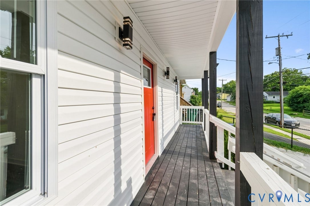 409 S Jefferson Street, Bolling, Petersburg, VA 23803 Front porch featuring white siding, a vibrant red entry door, dark wood-finish decking, and contemporary exterior lighting fixtures