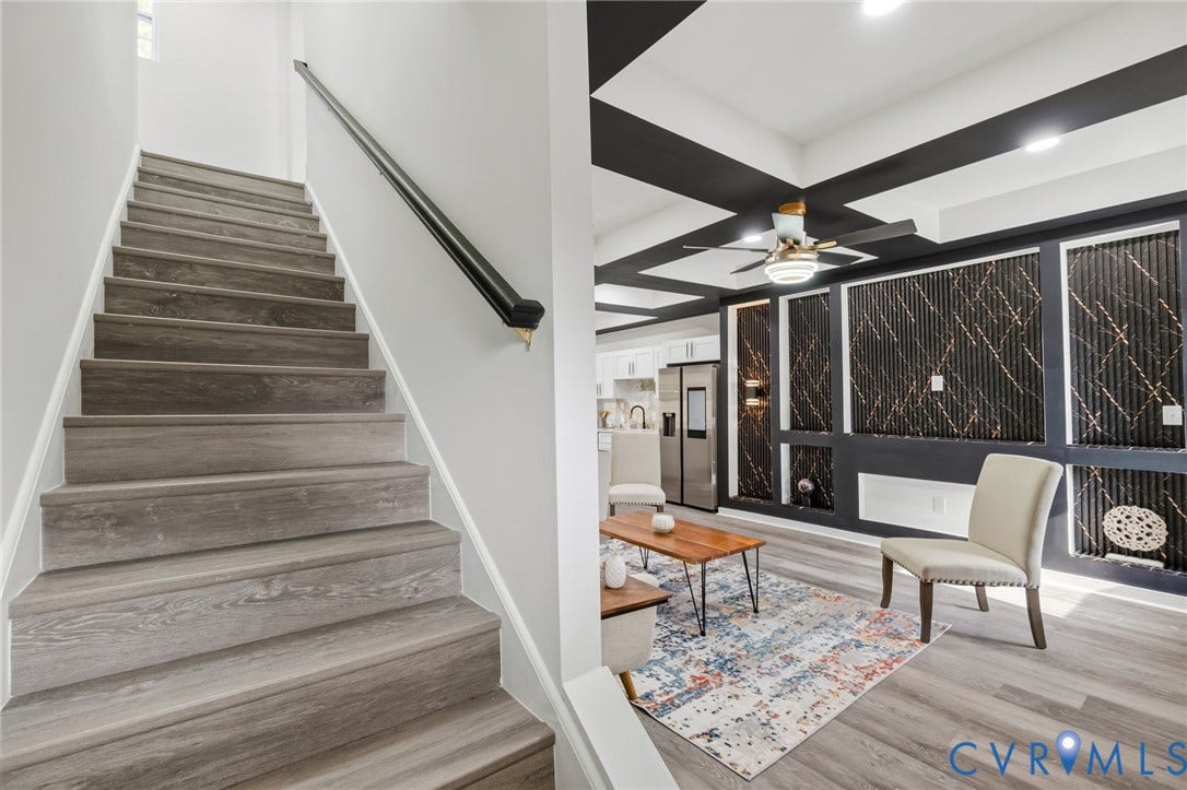 409 S Jefferson Street, Bolling, Petersburg, VA 23803 Modern staircase featuring wood-finish treads with crisp white walls and a sleek metal handrail, leading to a contemporary great room highlighted by coffered ceiling details, black structural beams, and built-in shelving with geometric paneling