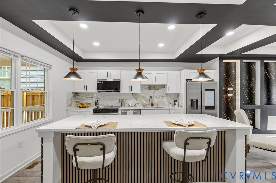 409 S Jefferson Street, Bolling, Petersburg, VA 23803 Contemporary kitchen featuring a large waterfall-edge island with fluted cabinetry, pendant lighting with metal shades, white cabinetry with integrated appliances, marble countertops, and a coffered ceiling with recessed lighting